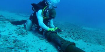 Budowniczy 2. klasy Christopher Farmer, przydzielony do podwodnego zespołu konstrukcyjnego (UCT) 2, instaluje stalowy pancerz wokół kabla dna morskiego na głębokości 100 stóp w ośrodku Pacific Missile Range Facility (PMRF) Barking Sands. Aut. Flota Pacyfiku Stanów Zjednoczonych, 14 sierpnia 2013 roku.